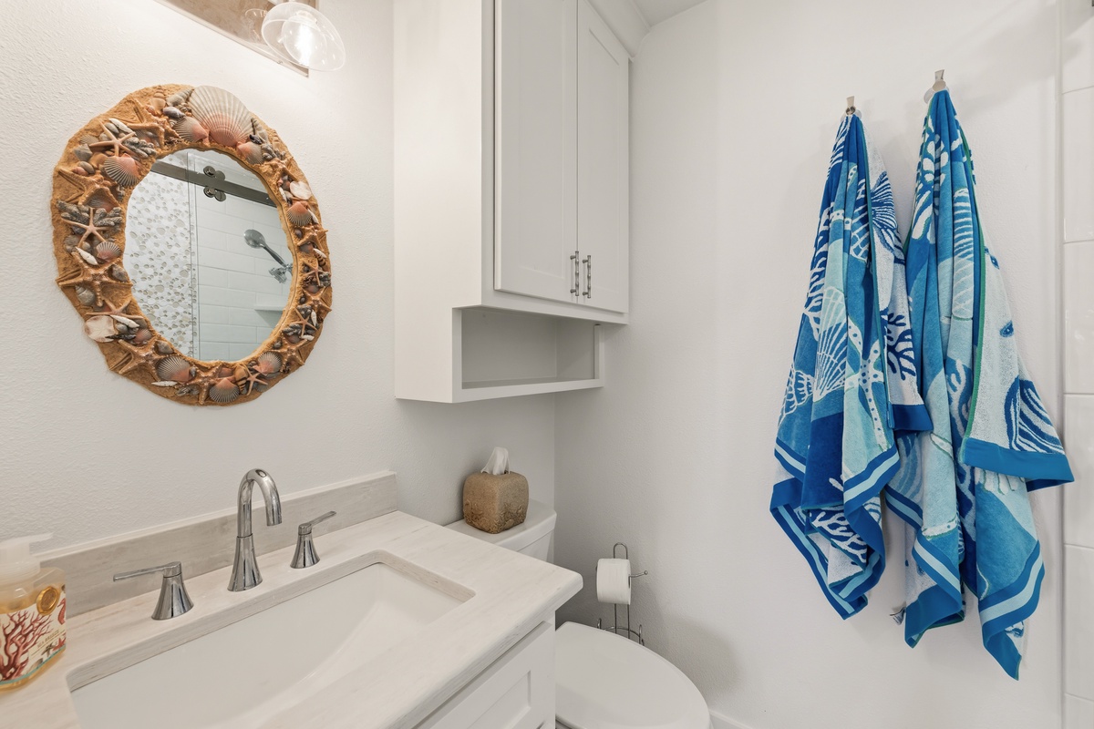Bright and clean, your bathroom features a seashell-framed mirror, fresh white cabinetry, and coastal-inspired towels that invite you to unwind after a day by the water.