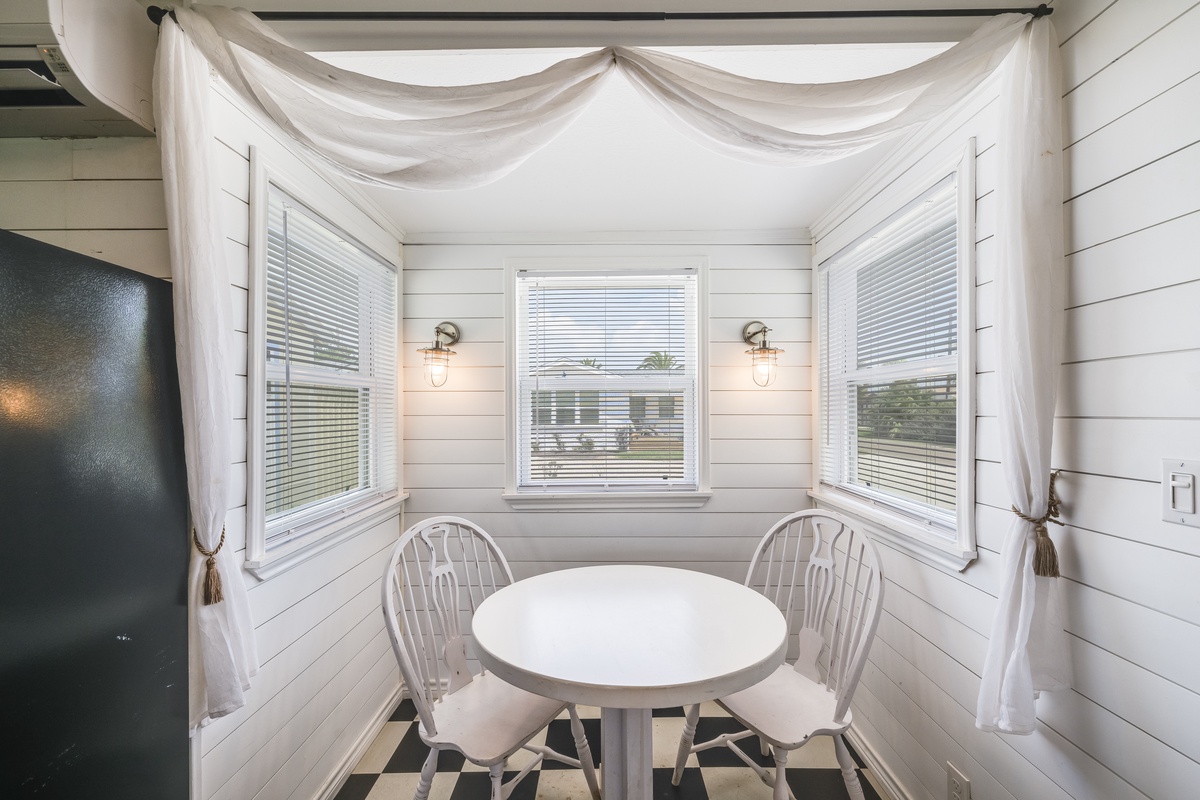 Gather for cozy meals in this charming breakfast nook, where soft sheer drapes frame bay windows and vintage-inspired sconces cast a warm, inviting glow.