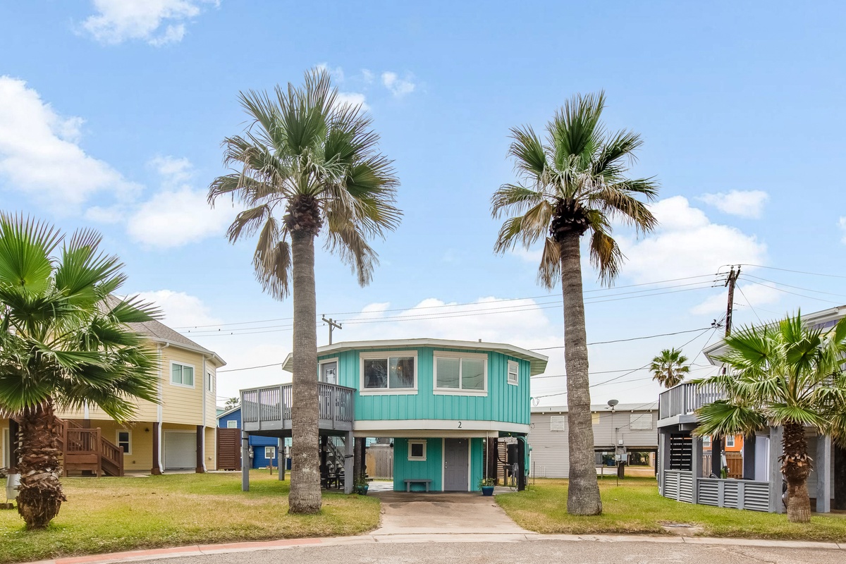 Charming turquoise beach house with towering palm trees and coastal neighborhood setting.