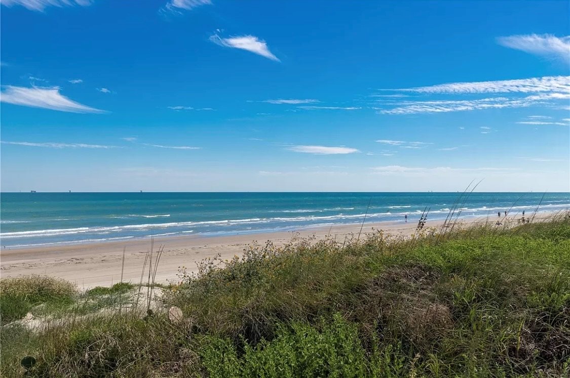Pristine coastline stretches along turquoise waters under brilliant blue skies, with natural dune grasses creating a peaceful seaside escape.