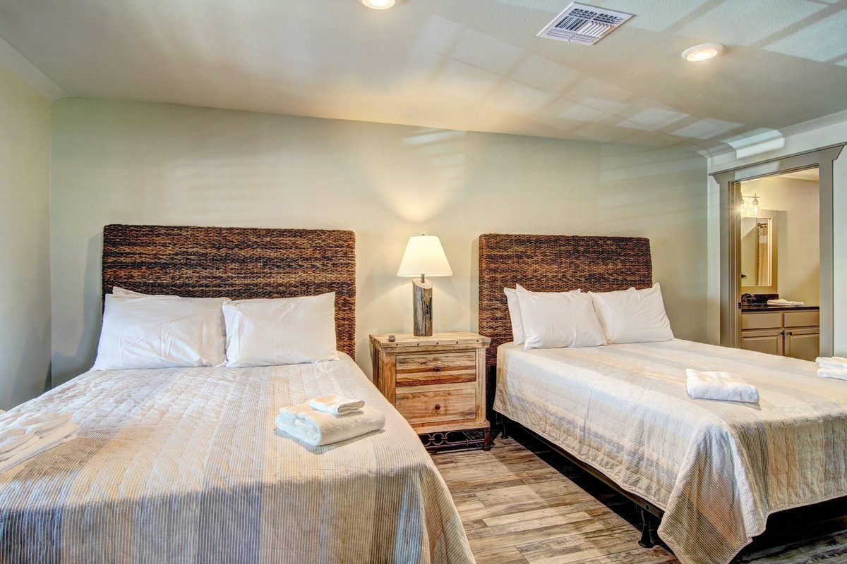 Sink into comfort with two plush beds featuring woven headboards and soft linens. Fresh towels await your arrival in this serene, well-appointed room.