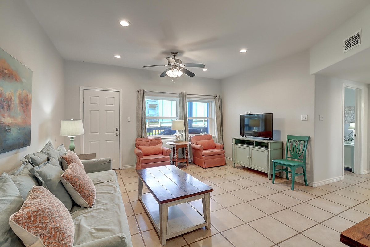 Relax in your bright, spacious living room with comfortable seating, large flat-screen TV, and cheerful coastal décor that invites you to unwind after beachside adventures.