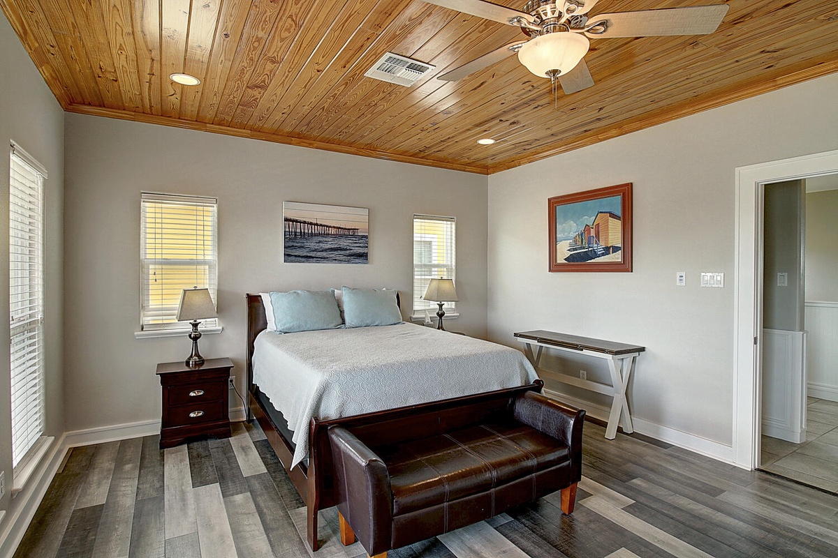 Unwind in your spacious bedroom featuring a stunning wood ceiling, comfortable seating bench, and coastal artwork that creates a serene retreat.