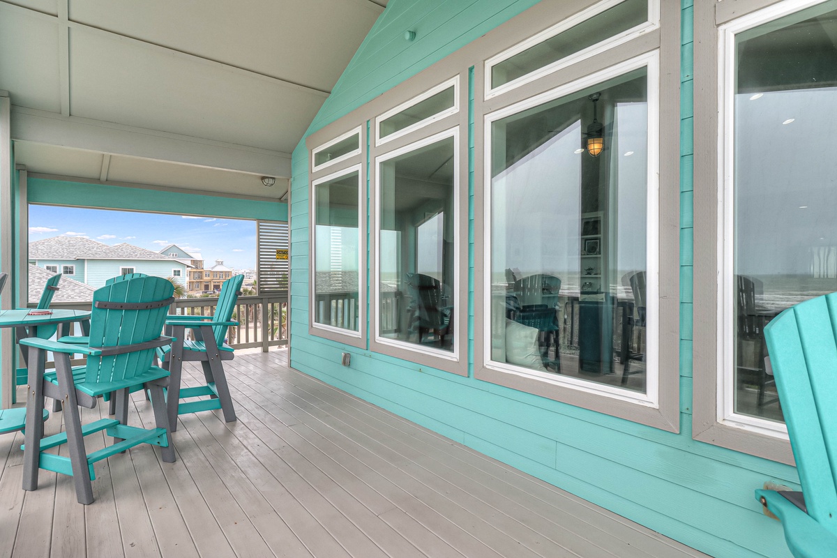 Relax on your private covered deck with turquoise Adirondack chairs and expansive windows showcasing coastal views.