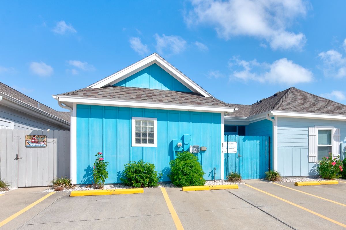 Charming turquoise beach cottage with white trim creates a cheerful coastal welcome under bright blue skies.