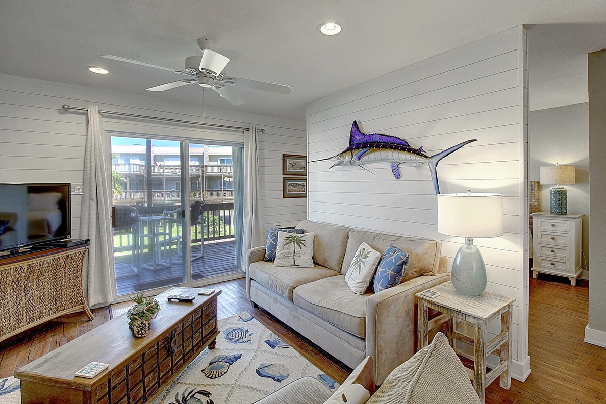 Relax in your coastal-themed living space with nautical decor, comfortable seating, and a peaceful balcony view.