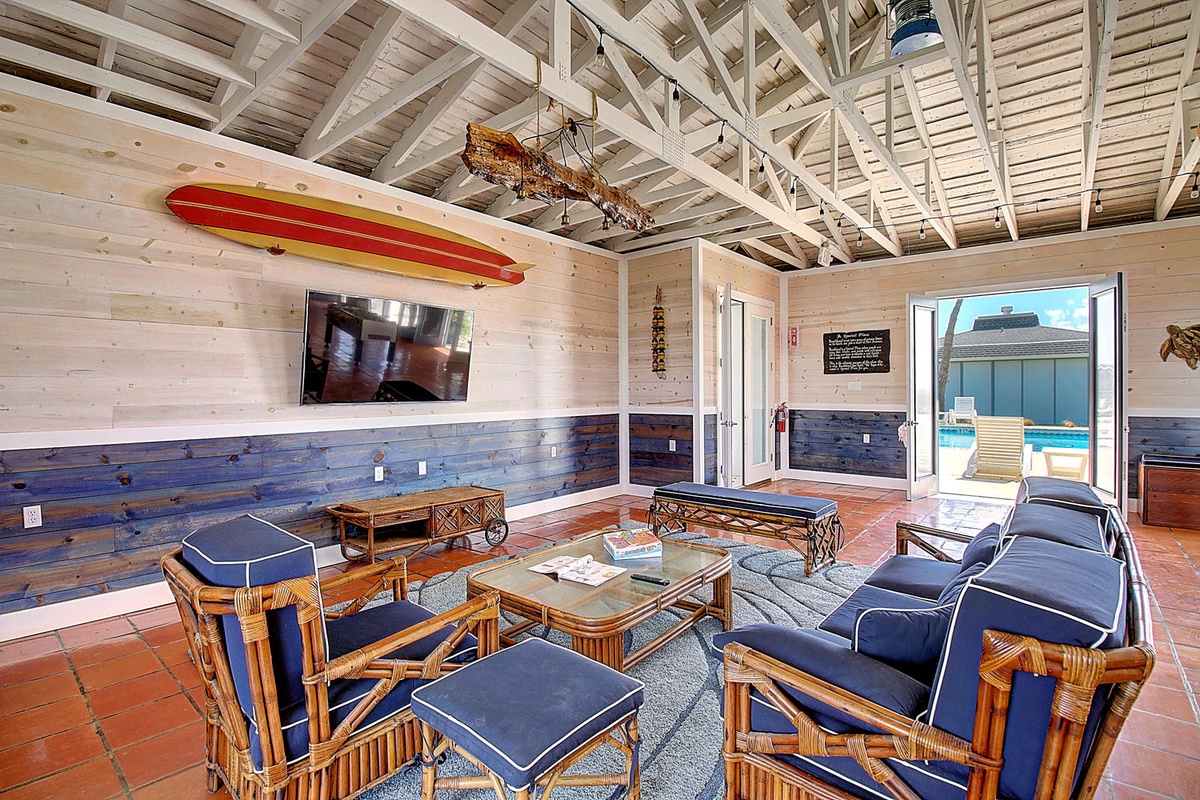 Relax in this coastal-inspired living space where vintage surfboards meet comfortable rattan seating under soaring wooden beams.