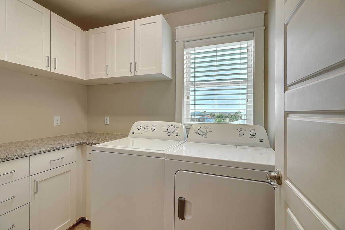 Your dedicated laundry room features modern washer and dryer with ample storage in crisp white cabinetry.