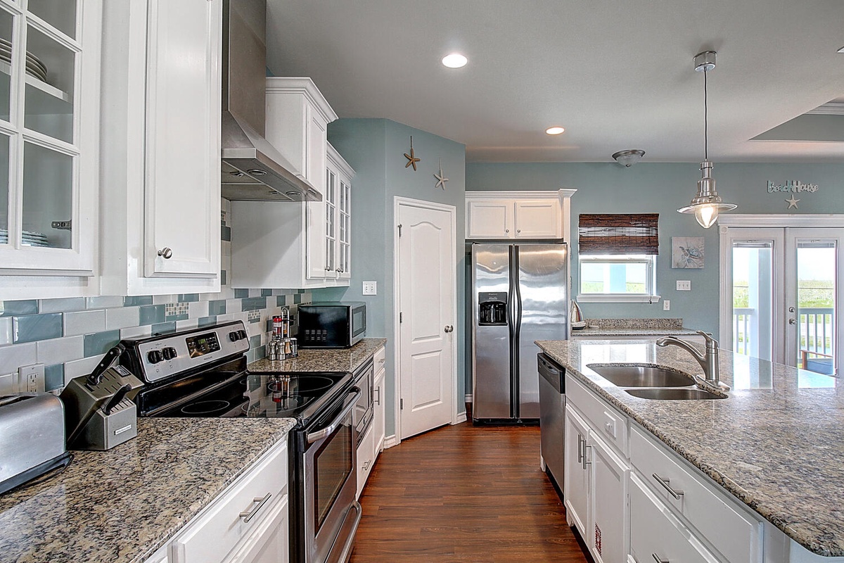 Cook your favorite meals in this spacious coastal kitchen with granite counters, stainless steel appliances, and beautiful tile backsplash—your perfect vacation culinary haven.