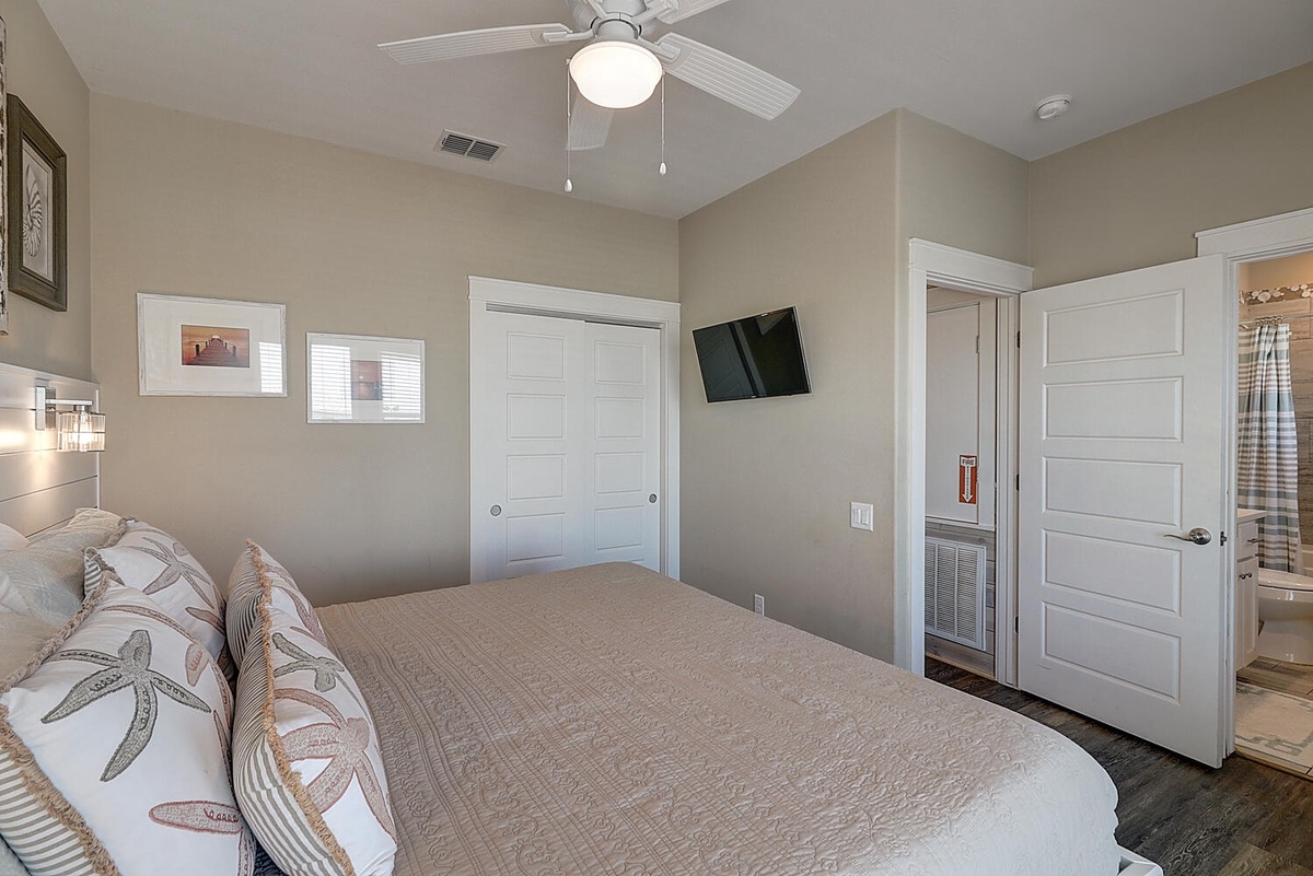 Unwind in your peaceful bedroom featuring a plush bed, ceiling fan, and wall-mounted TV for cozy evenings.