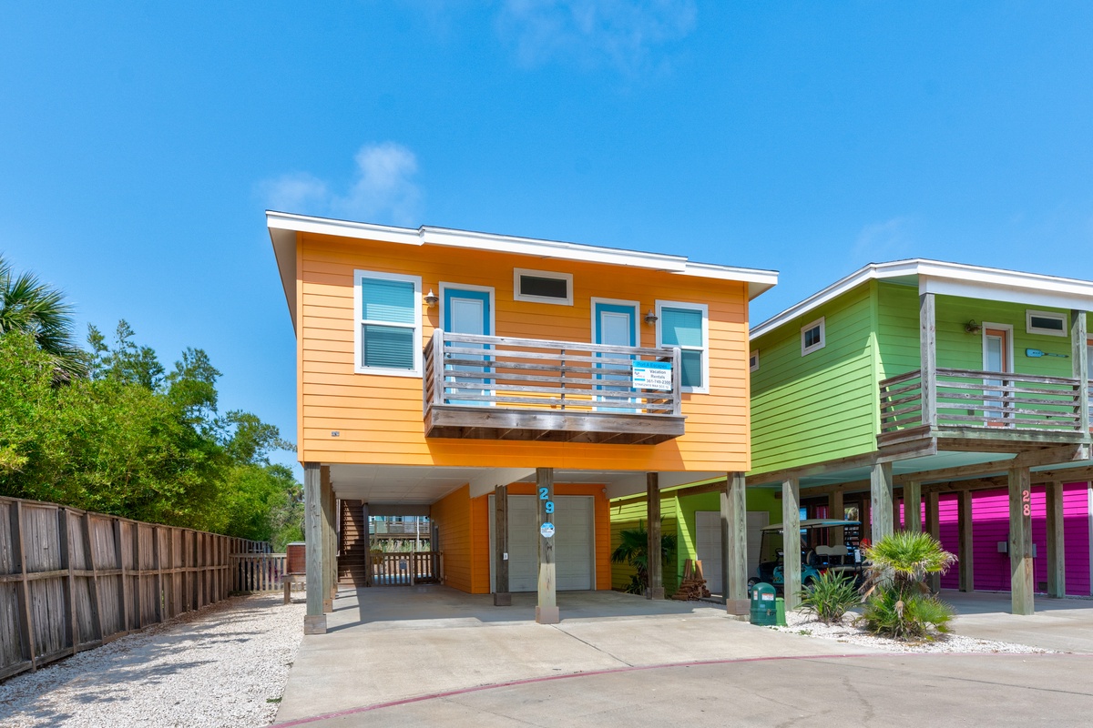Bright orange beach house on stilts features modern design with spacious covered parking and tropical landscaping in colorful coastal neighborhood.
