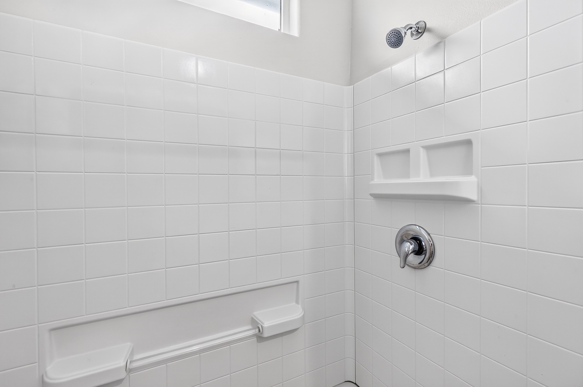 The shared bathroom features a clean, tiled tub and shower combination with built-in shelving for added convenience.