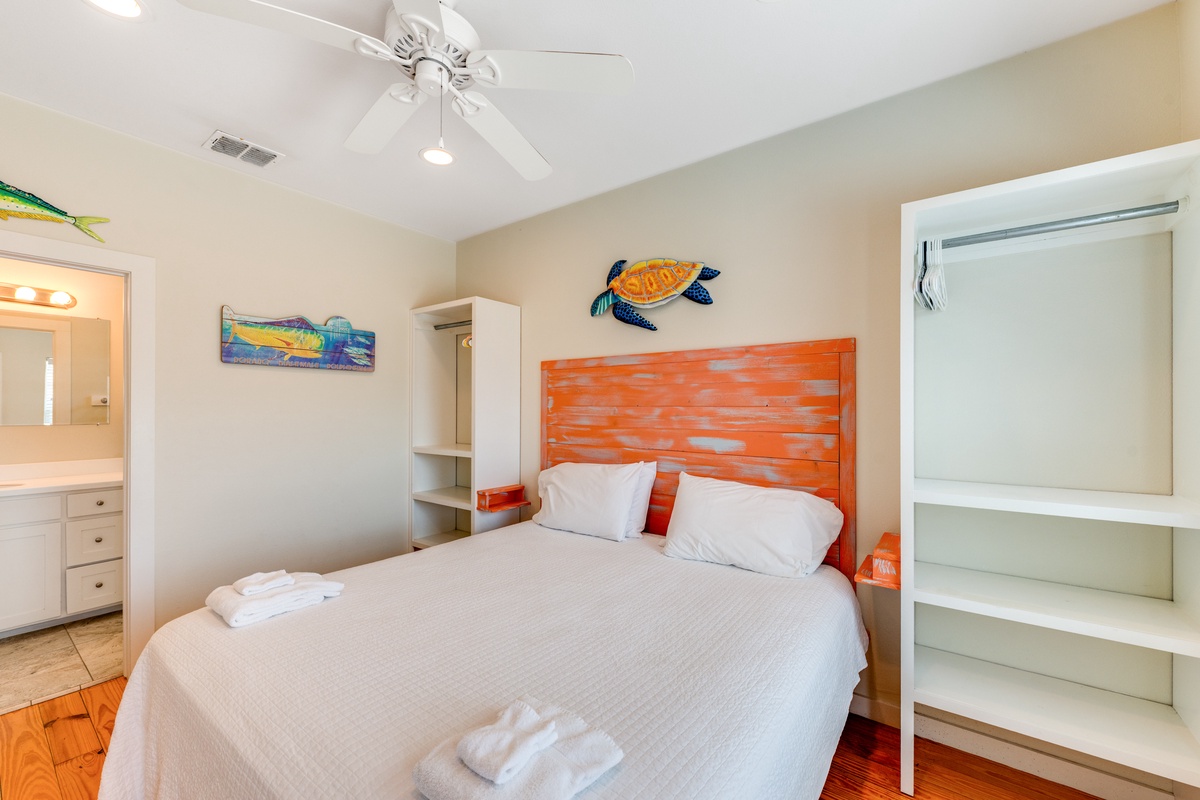 Drift off to sleep under the gentle ceiling fan breeze in your coastal-themed bedroom with vibrant orange accents and ocean art.