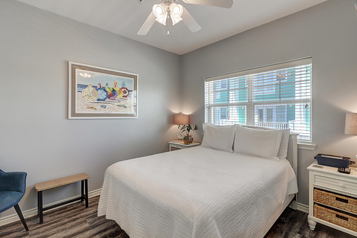 Sink into soft linens in your peaceful bedroom retreat with coastal artwork and city views through bright windows.