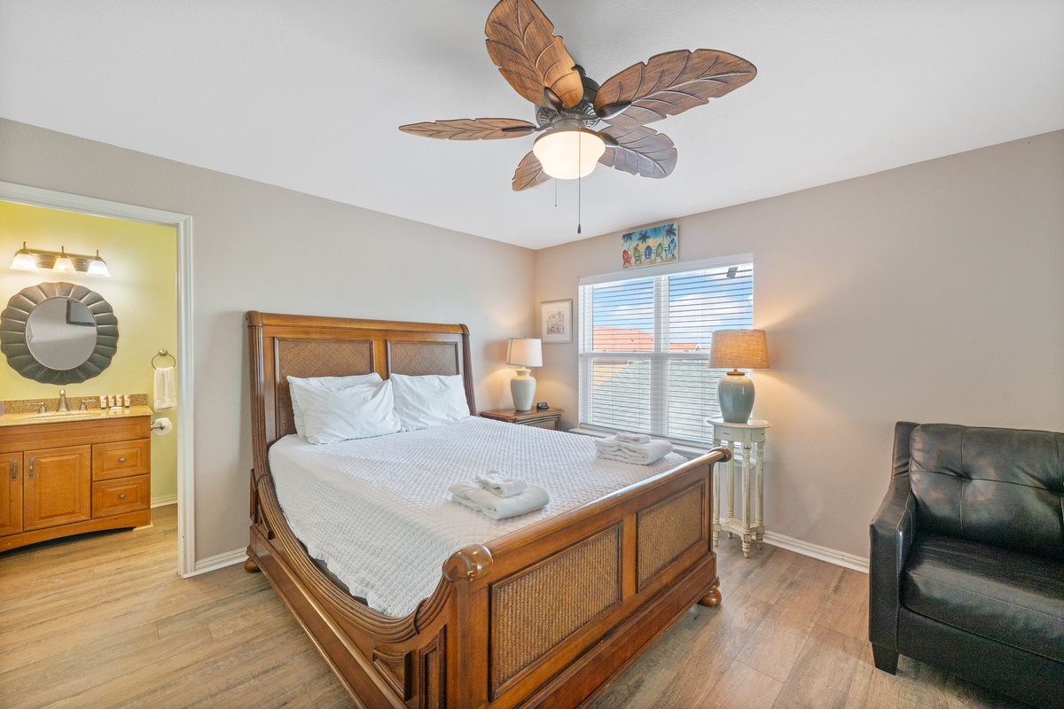 Unwind in your tropical-themed bedroom featuring a plush bed, leaf-motif ceiling fan, and serene coastal ambiance.