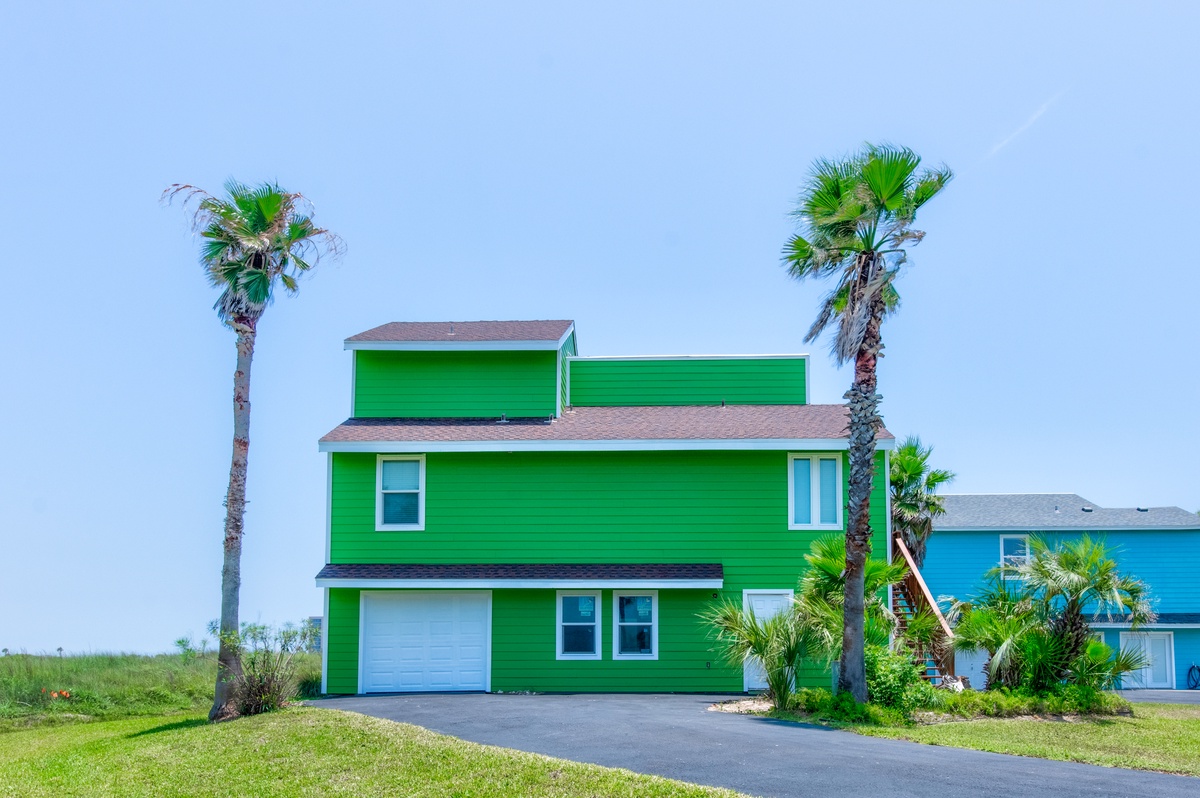 Bright green coastal home with palm trees and garage, situated in a tropical neighborhood near the beach.