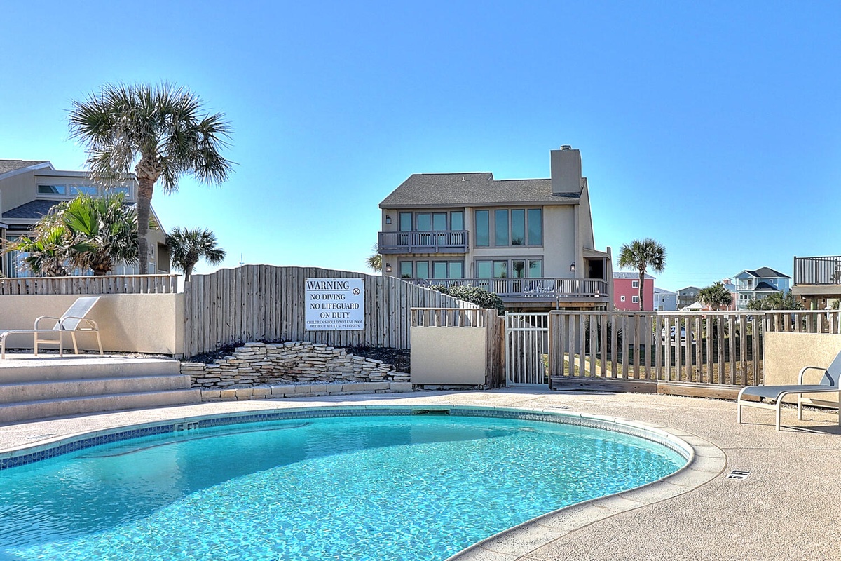 Sparkling pool surrounded by coastal homes and swaying palms creates the perfect vacation setting.