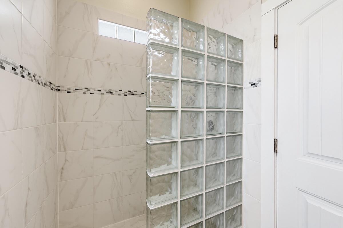 Step into your private sanctuary with elegant marble-look tiles and a stylish glass block wall that brings in soft natural light for a spa-like experience.