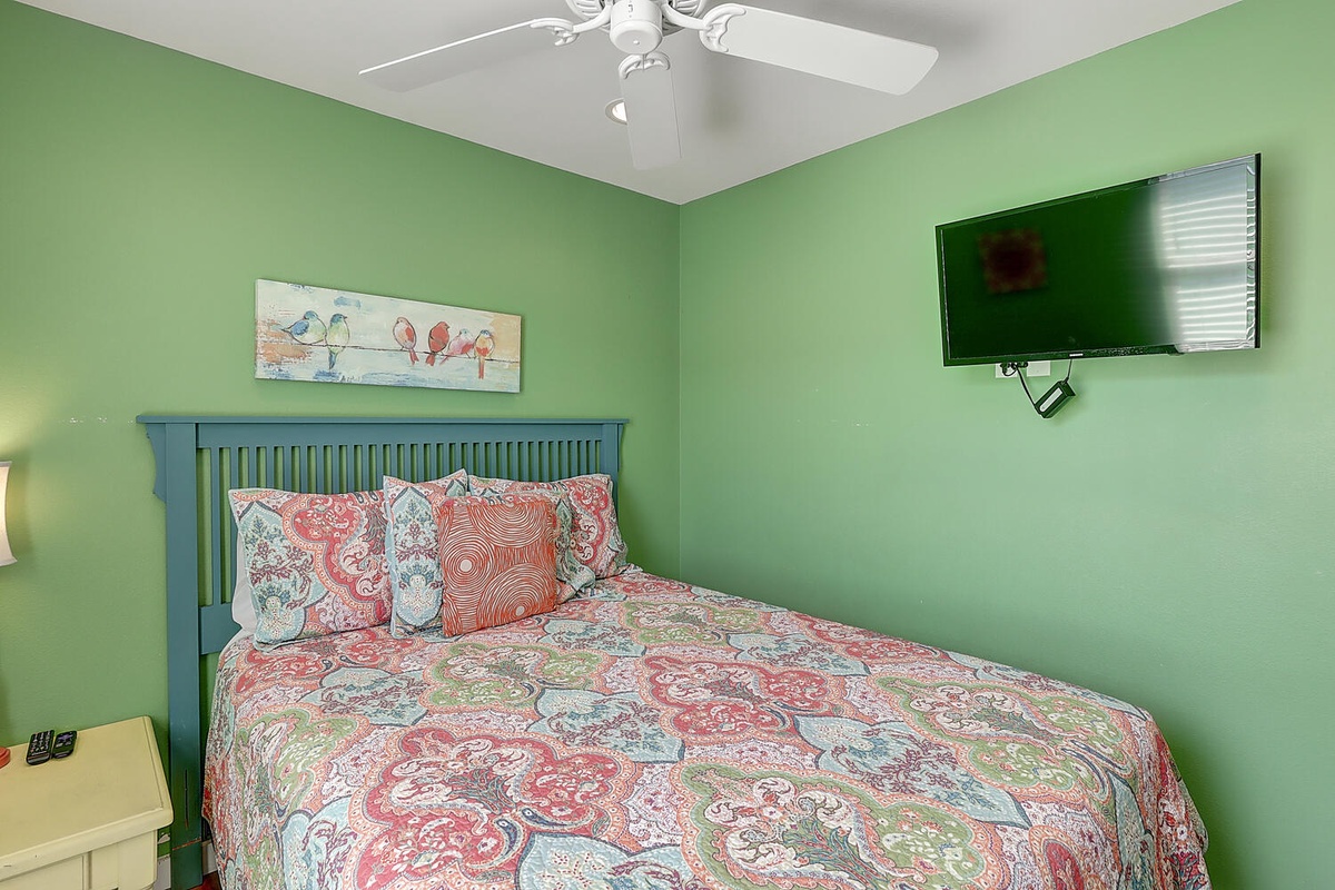 Relax in your cheerful bedroom with vibrant paisley bedding, wall-mounted TV for cozy movie nights, and ceiling fan for perfect comfort.