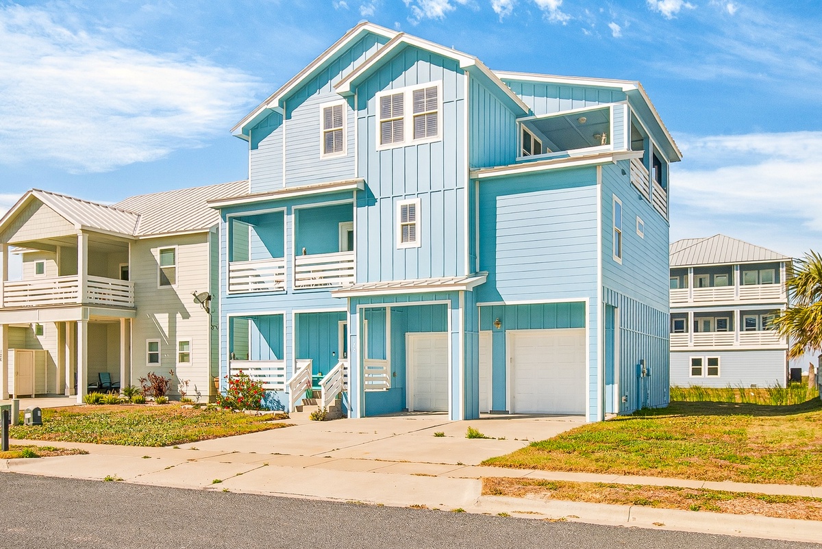Charming coastal vacation home featuring bright turquoise and white exterior with multiple levels and covered parking in a peaceful residential neighborhood.
