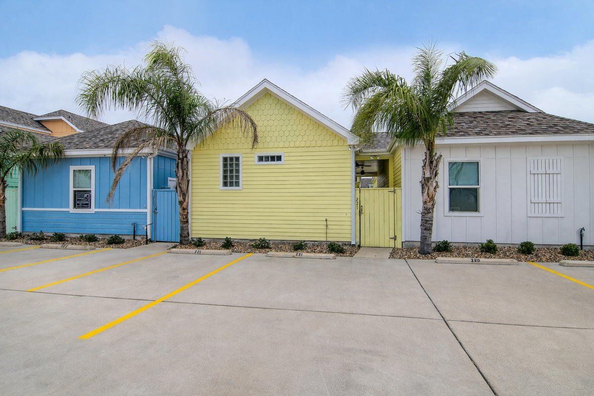 Colorful beach-style cottages with palm trees and dedicated parking create a cheerful tropical resort setting.