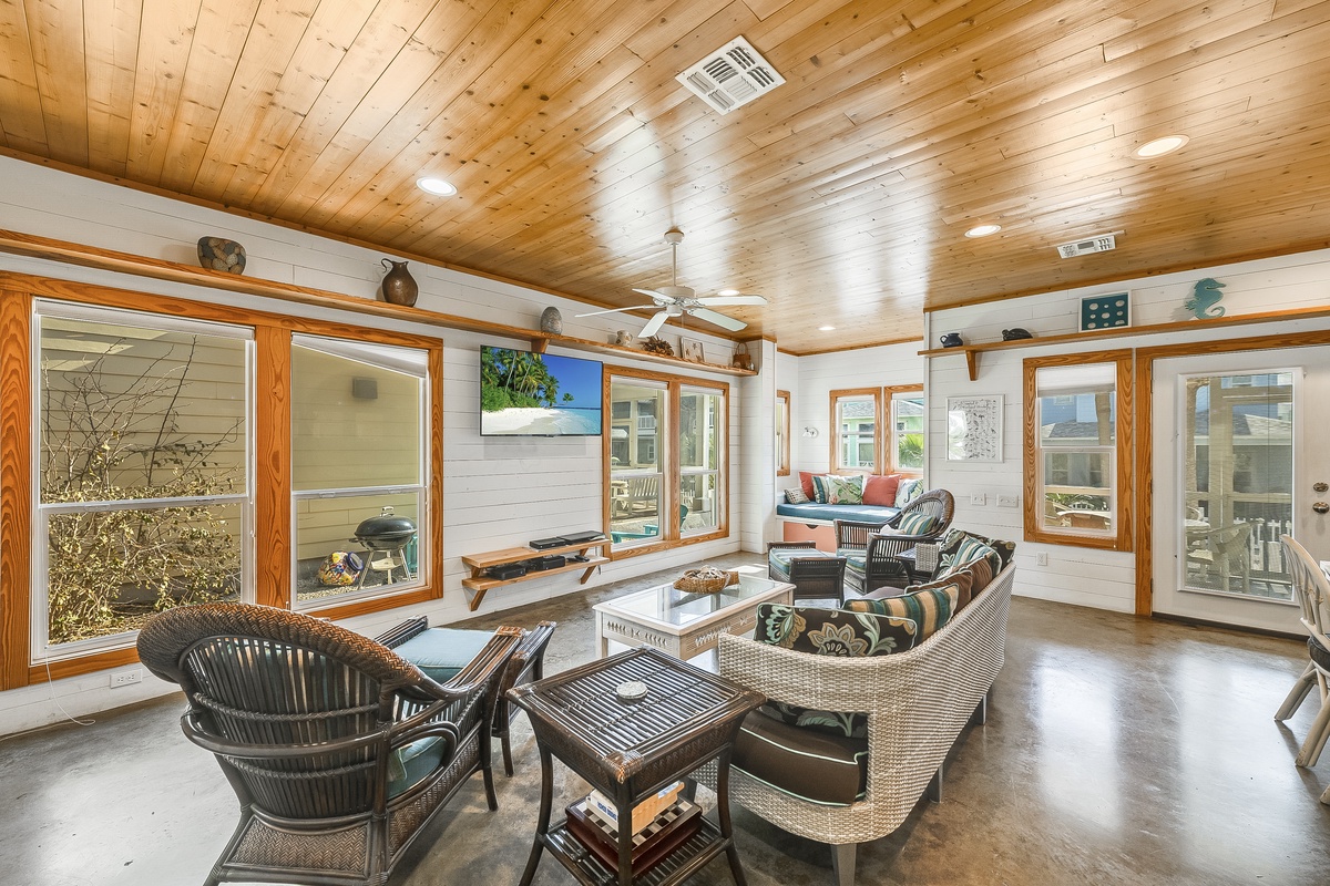 Unwind in your bright, wood-beamed living room with cozy seating, modern TV, and large windows showcasing peaceful garden views.