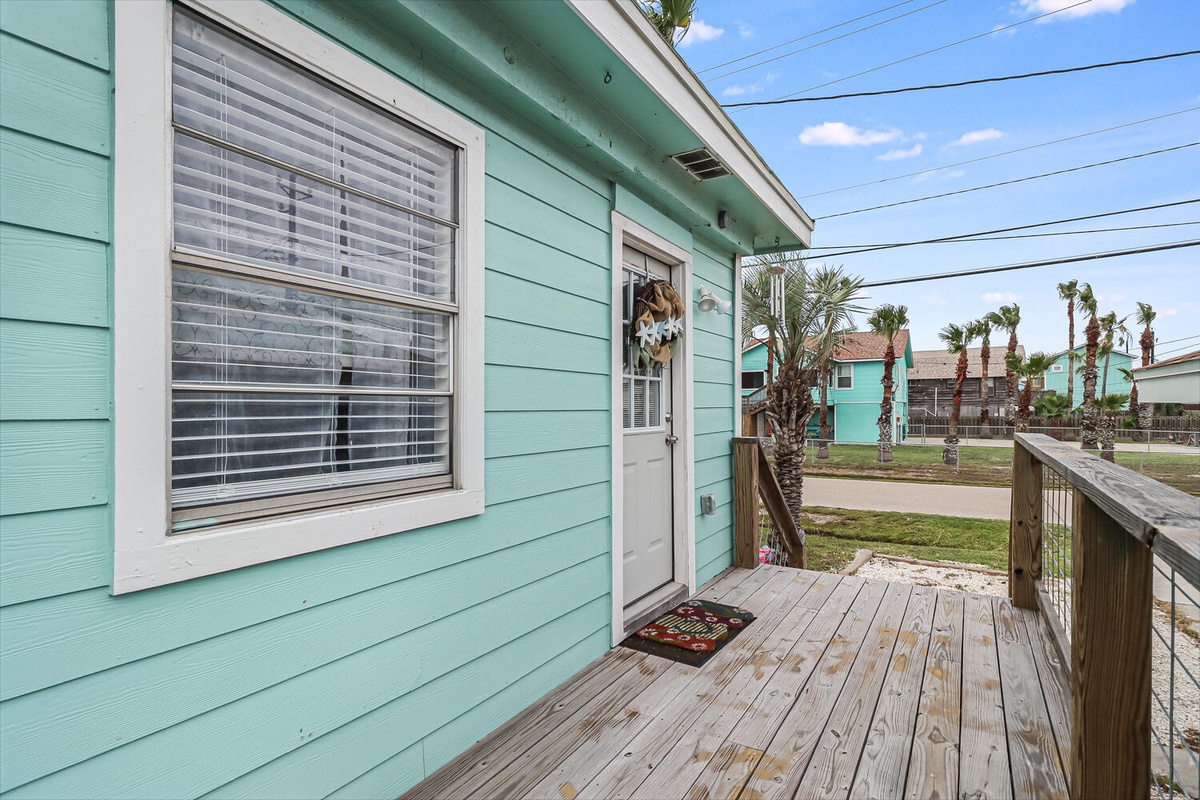 Charming seafoam green cottage with welcoming front porch and tropical surroundings in a peaceful residential neighborhood.