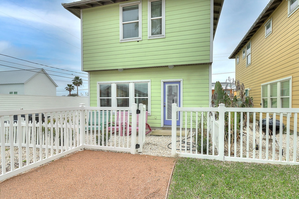 Cheerful green two-story home with white picket fence in a colorful coastal neighborhood setting.