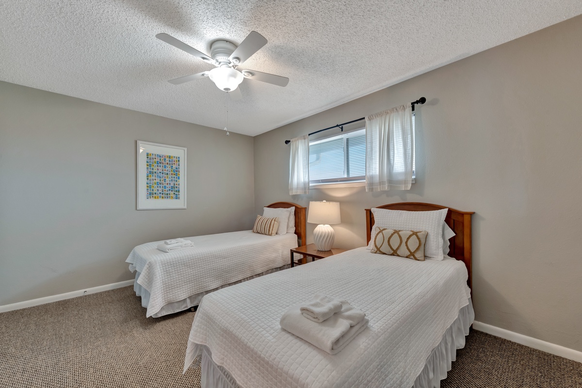 Relax in your cozy twin bedroom with fresh linens, gentle ceiling fan, and warm natural light streaming through the window.