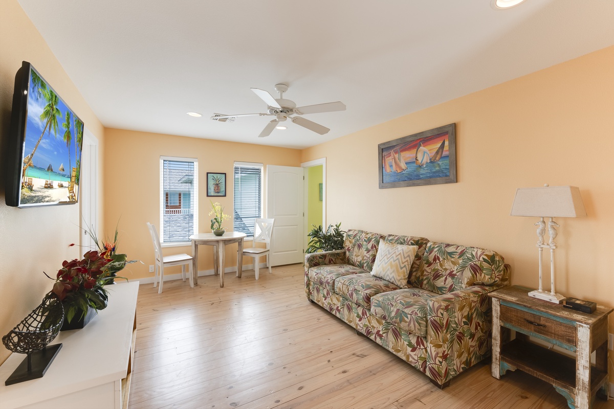 Relax in your tropical-themed living room with colorful floral sofa, dining nook, and entertainment center—your perfect home base.