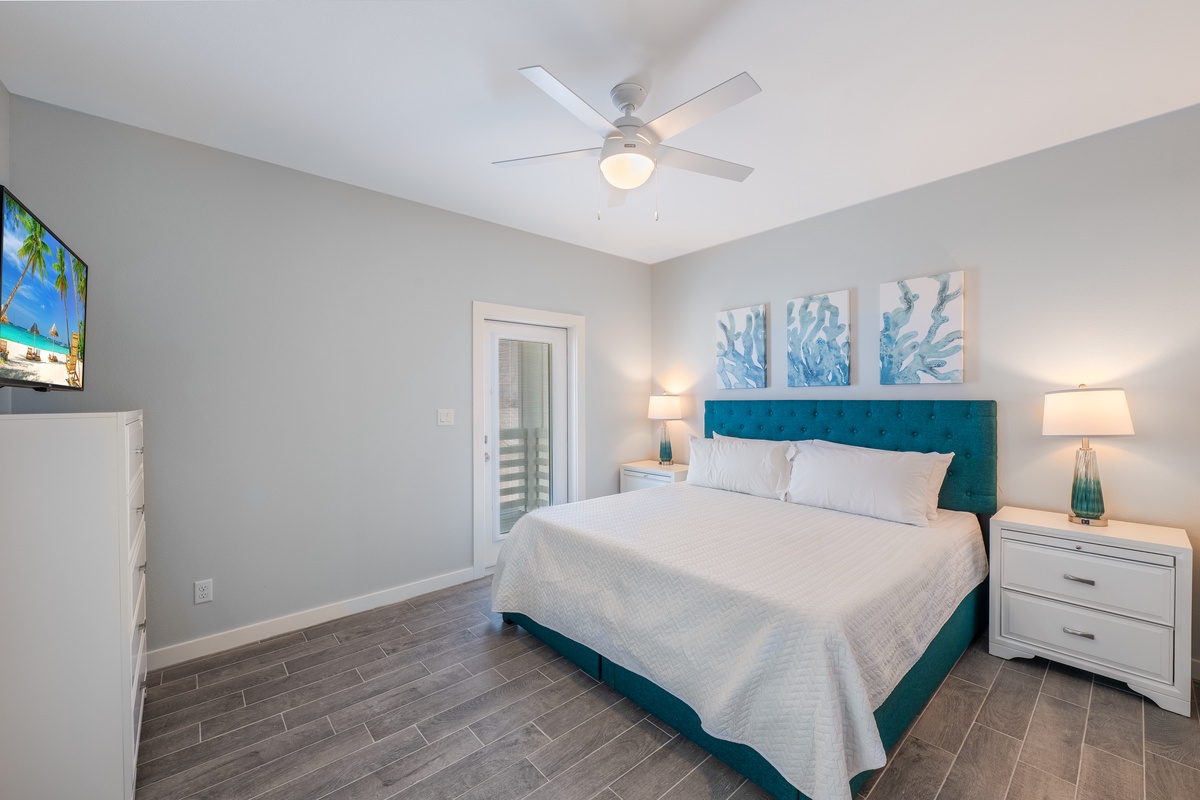 Drift off in this serene bedroom featuring a plush teal headboard, crisp linens, and calming coastal artwork above your bed.