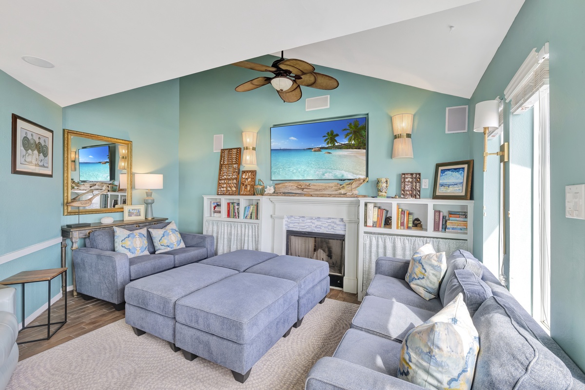 Relax in this serene coastal living room with comfortable blue seating, tropical ceiling fan, and warm fireplace for perfect year-round comfort.