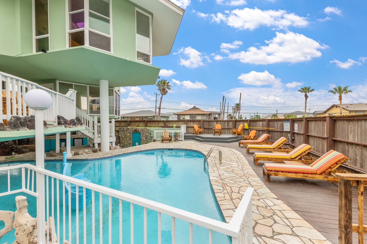 Vibrant green property featuring a sparkling pool with comfortable loungers and tropical palm trees under sunny skies.