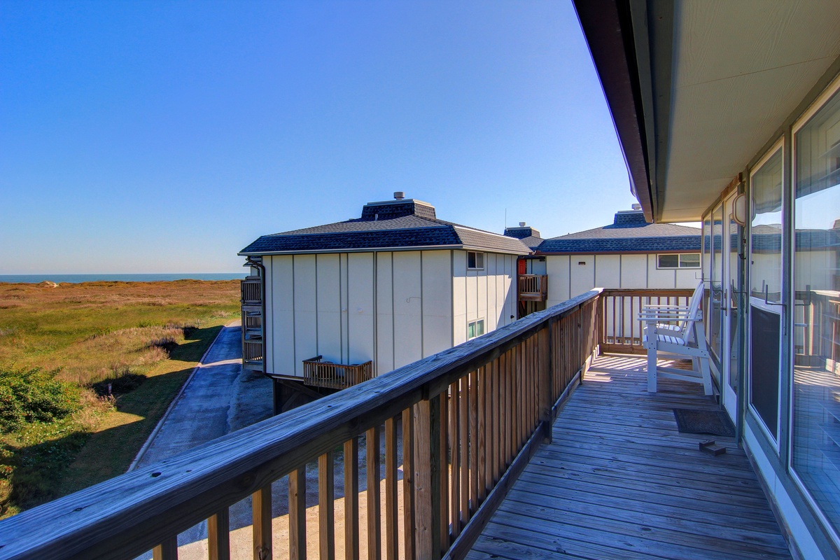 Expansive wooden deck with ocean views and neighboring buildings in a coastal resort setting.