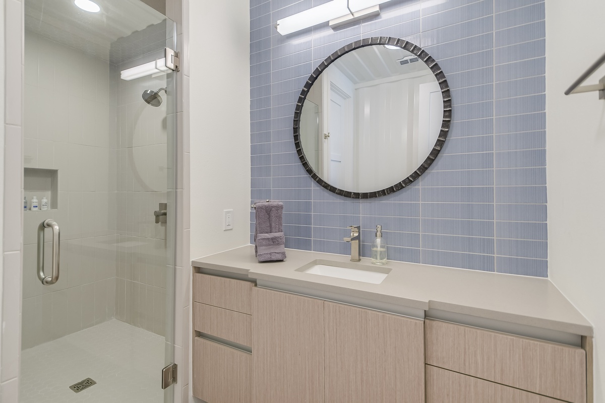 Your private bathroom features a spacious walk-in shower and sleek vanity with stylish blue tile accents.