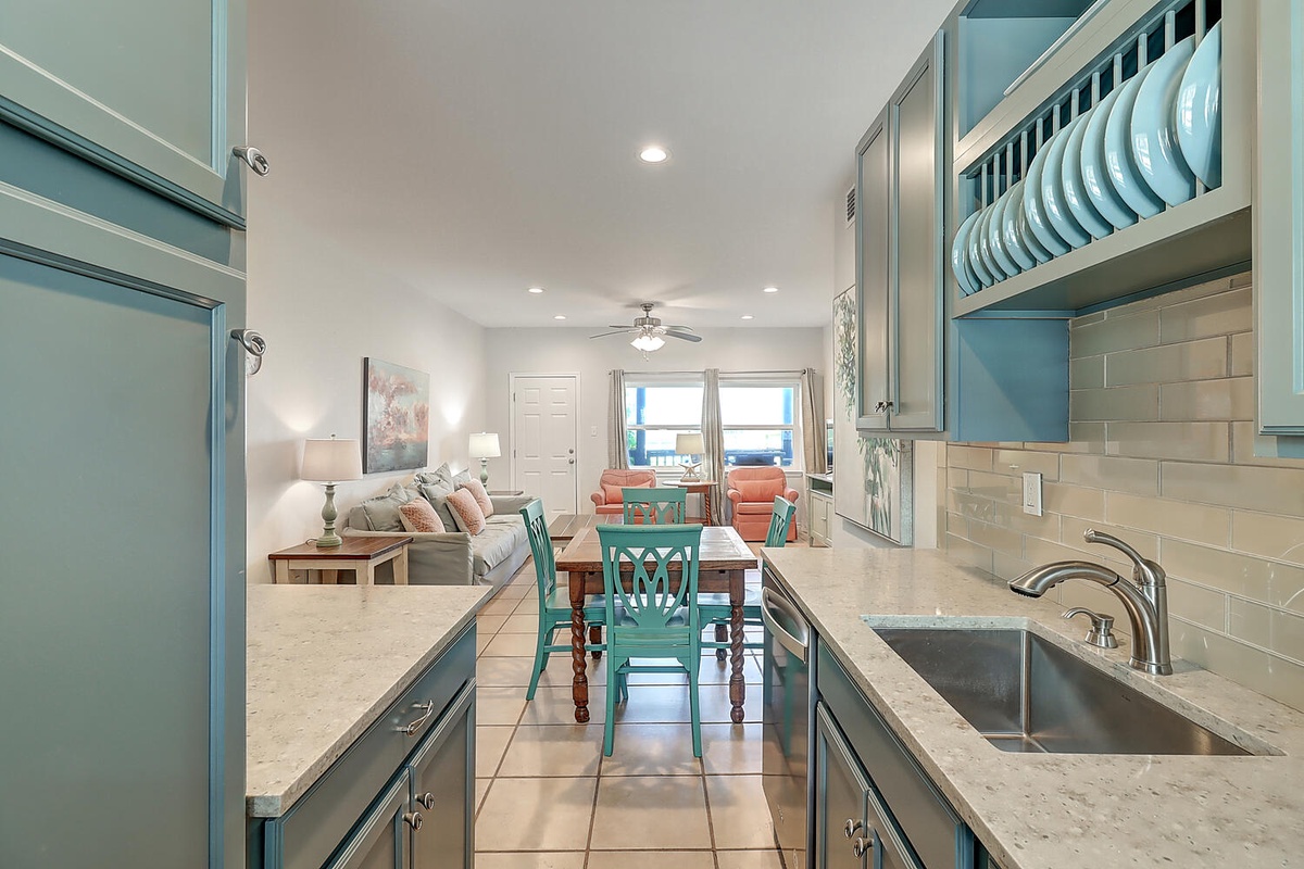 Your bright coastal kitchen opens to a welcoming living space with soft turquoise accents and marble countertops for easy meal prep.