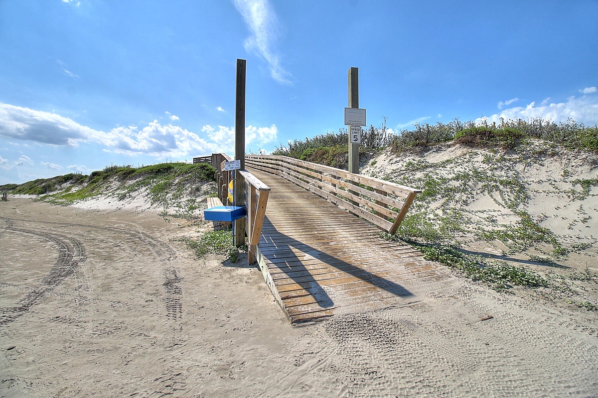 A wooden boardwalk leads through coastal dunes, providing easy access to the sandy beach area.