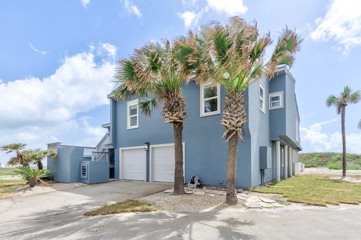 Modern blue beach house with palm trees and two-car garage in coastal setting.