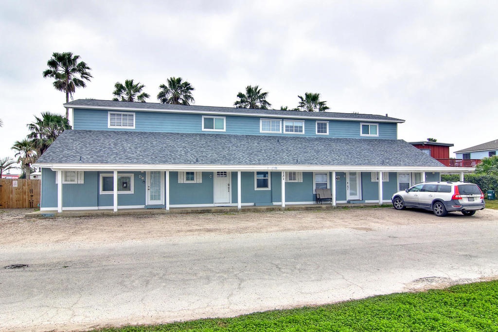 Two-story blue vacation rental property with tropical palm trees and convenient parking in a quiet residential setting.
