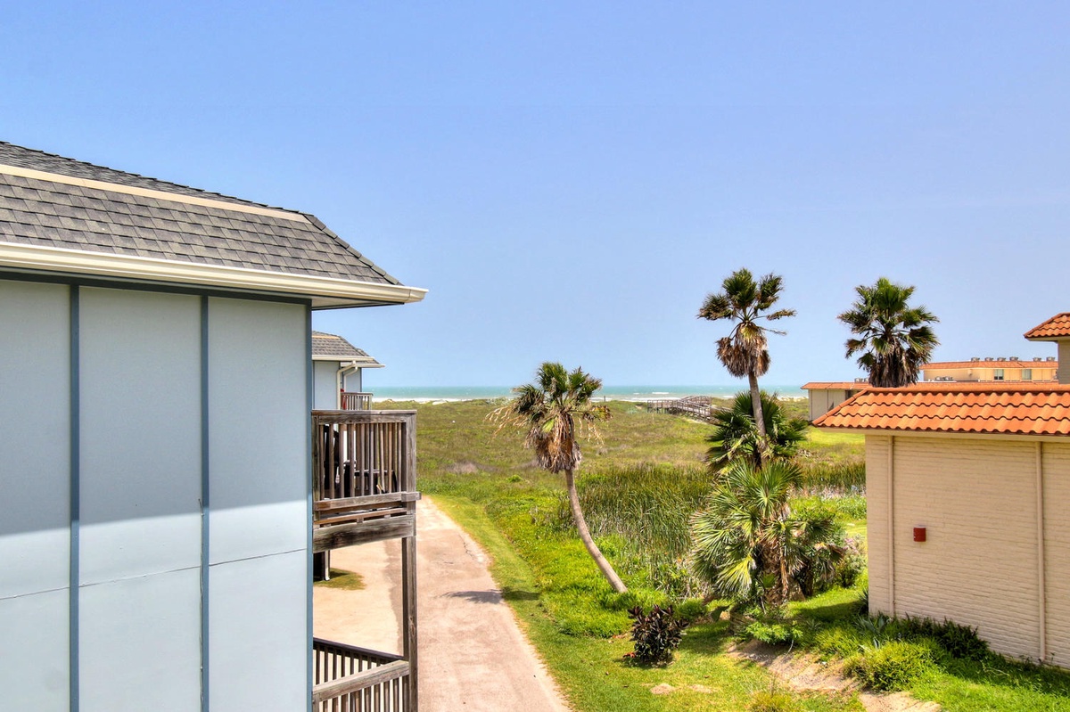 Coastal property with tropical landscaping and beach access nearby, featuring palm trees and ocean views.