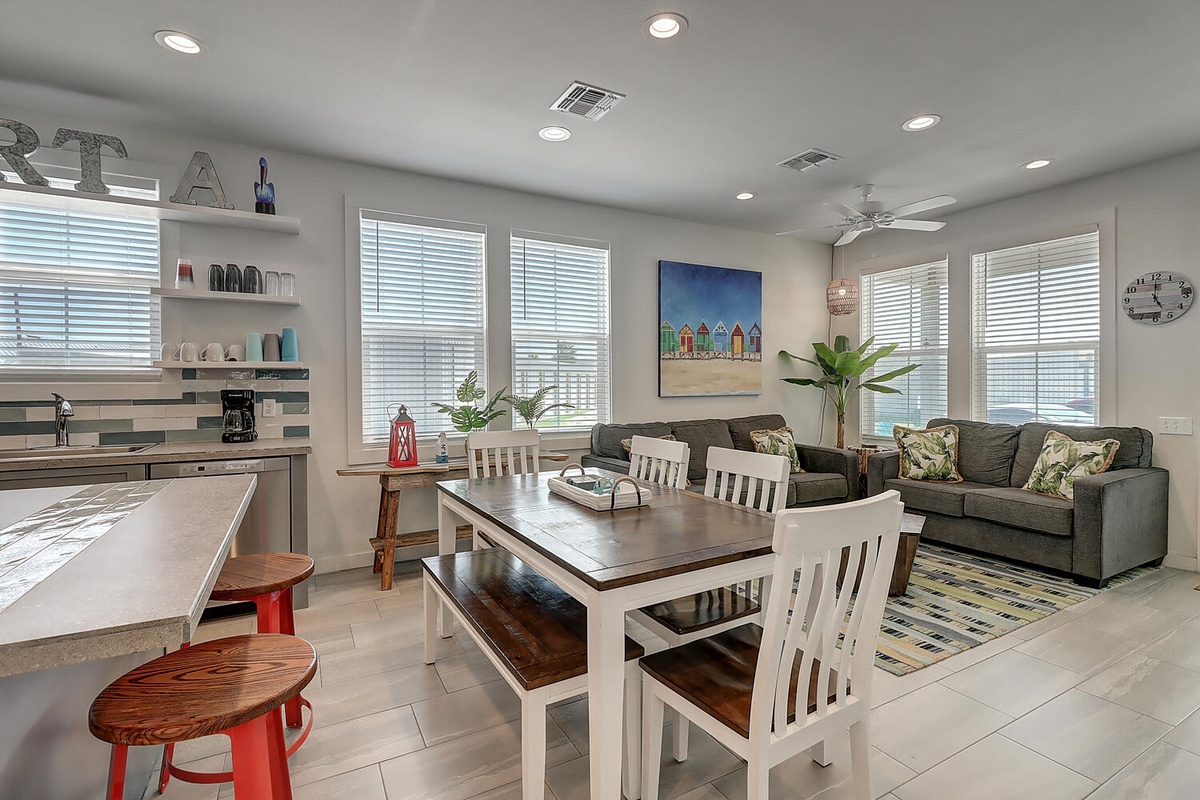 Your bright, open living space seamlessly blends kitchen, dining, and relaxation areas with natural light streaming through windows.