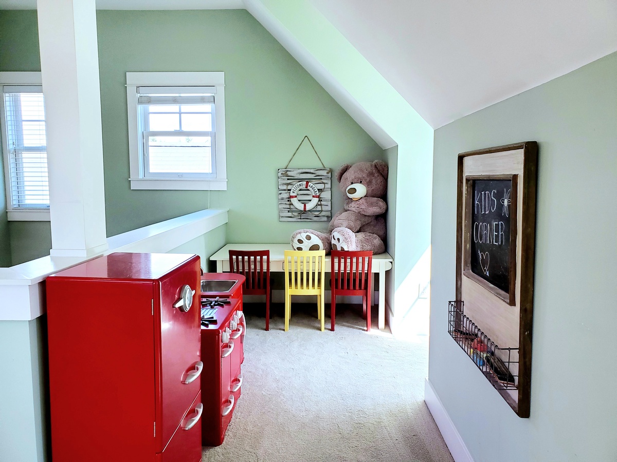 Kids corner filled with stocked play kitchen, Legos, cars, toys, chalkboard and craft table