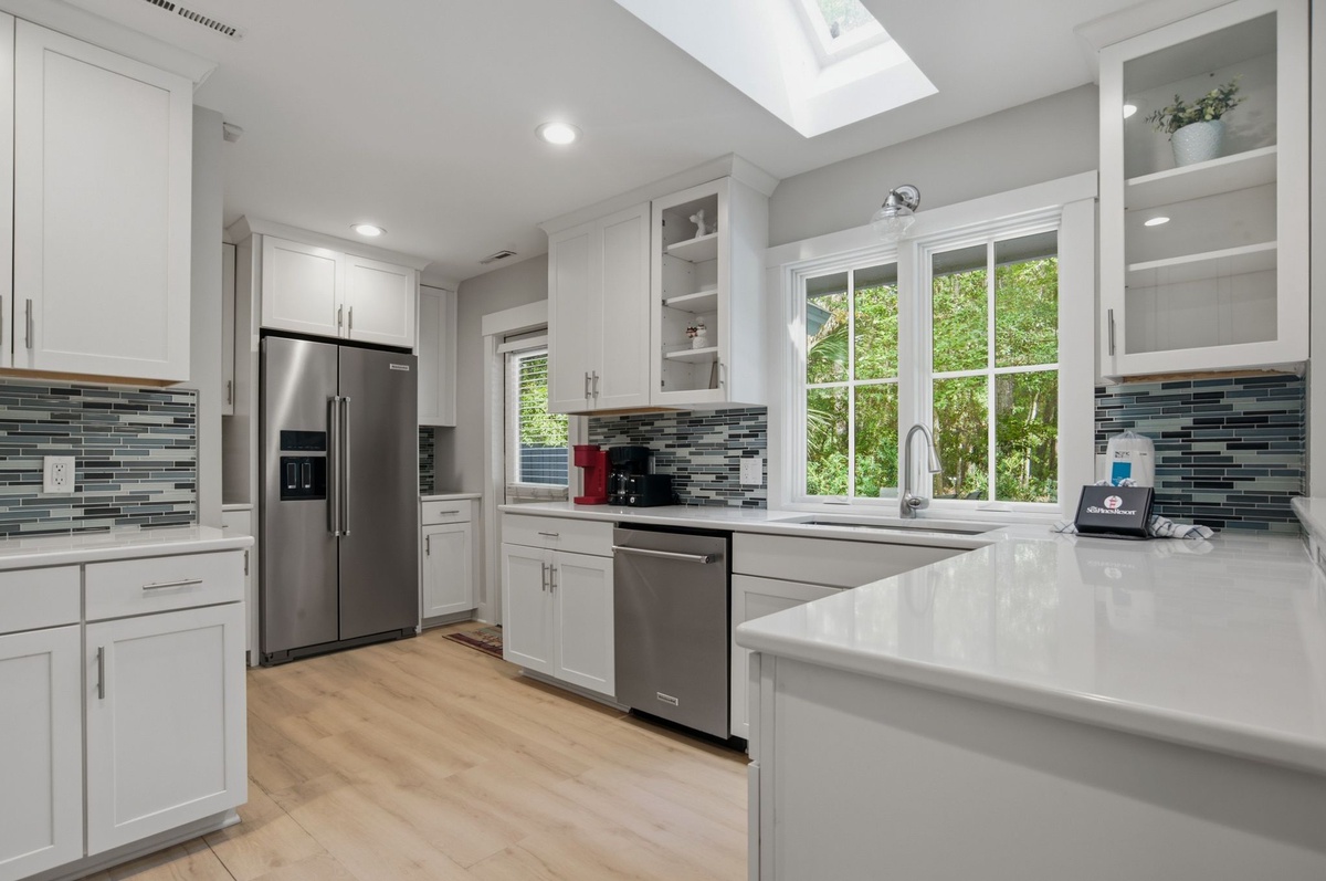 Step into your bright, fully equipped kitchen with sleek white cabinetry, stainless appliances, and a skylight overhead that fills the space with natural light as you prepare your meals..