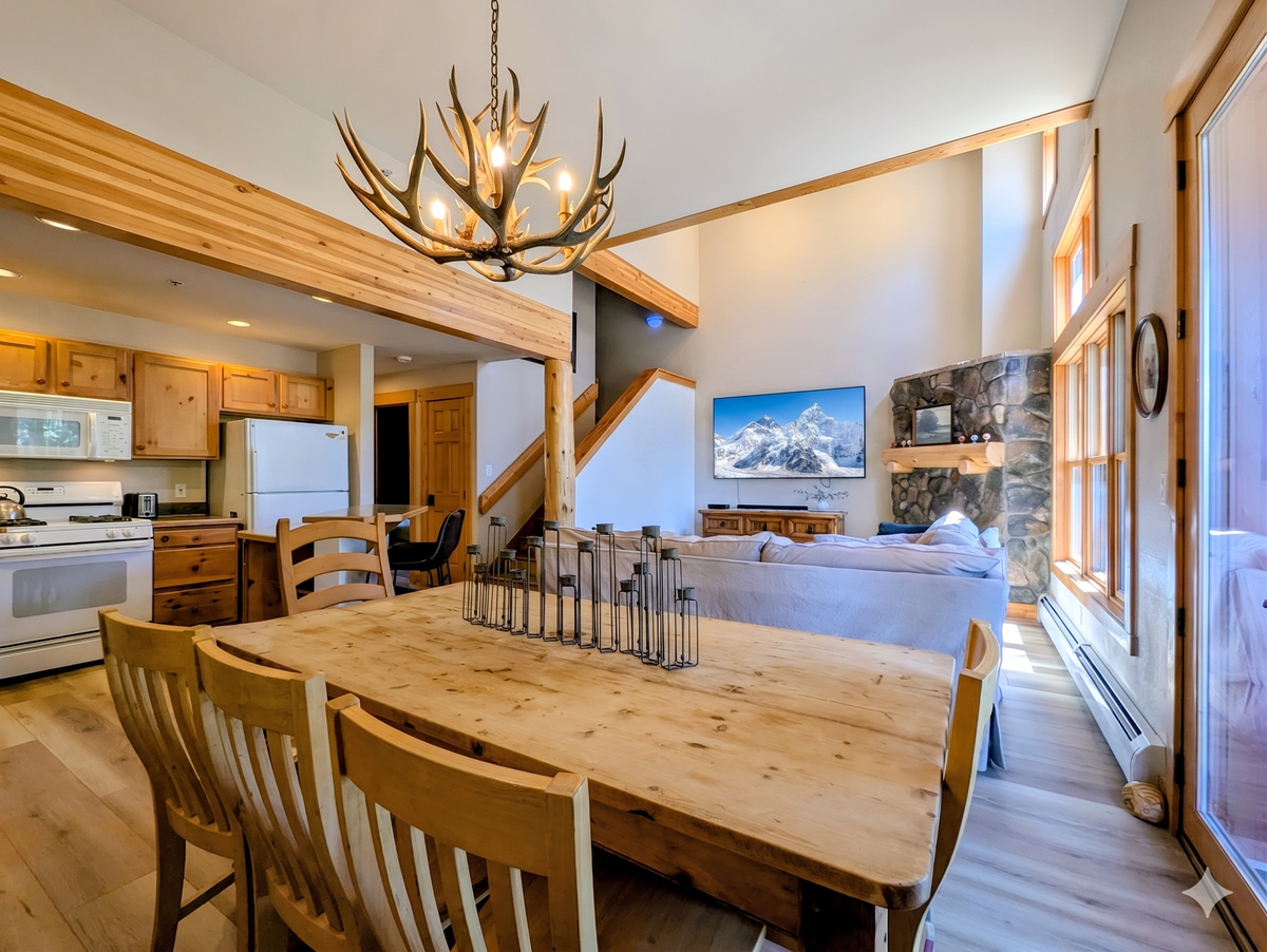 Gather around a spacious dining table under a striking antler chandelier, with your cozy living area and stone fireplace just steps away, perfectly blending rustic charm with modern mountain comfort.