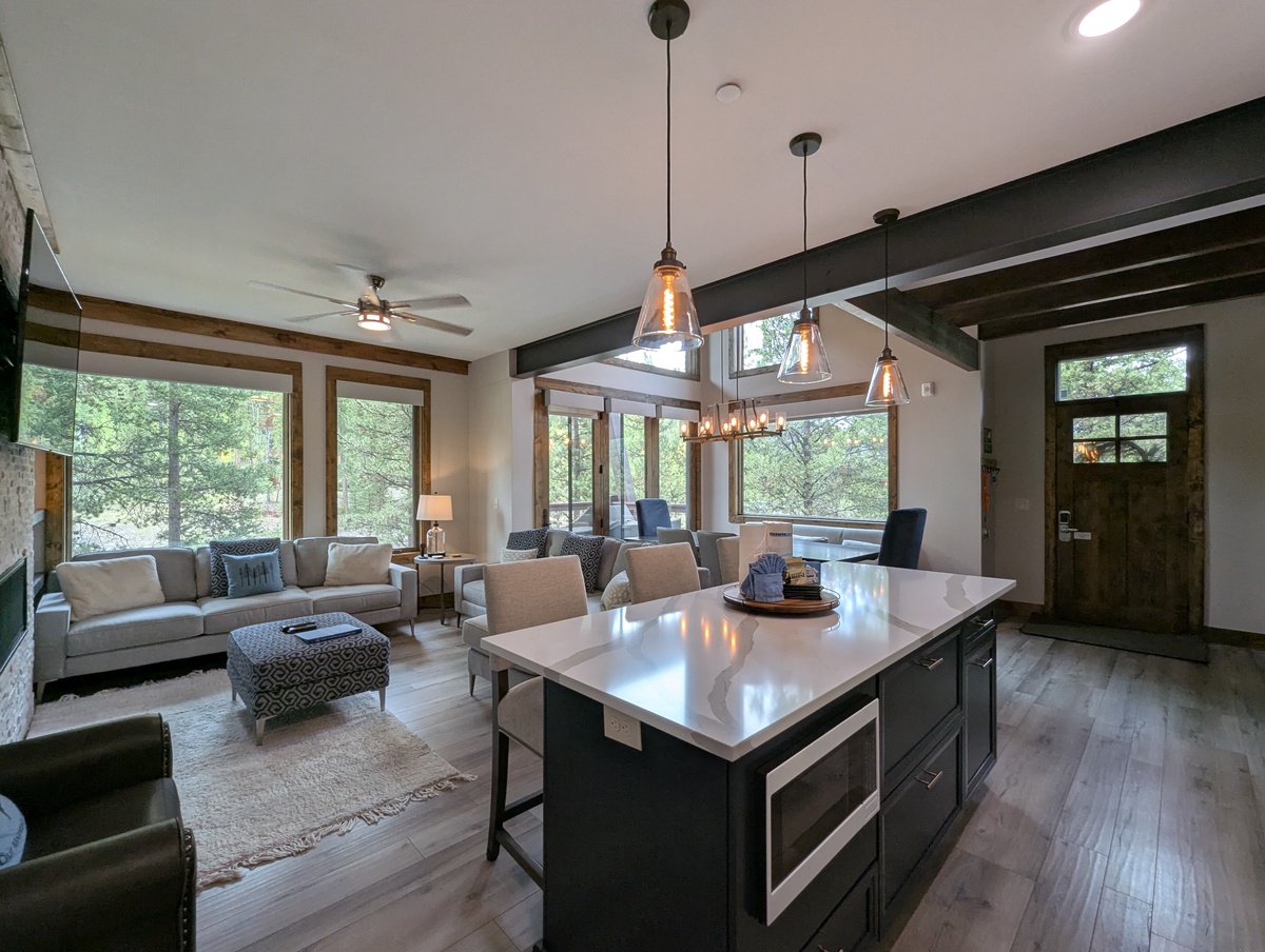 Bright, open-concept retreat with walls of windows framing peaceful forest views. Chef's kitchen island flows seamlessly into a cozy living area, perfect for gathering and unwinding.