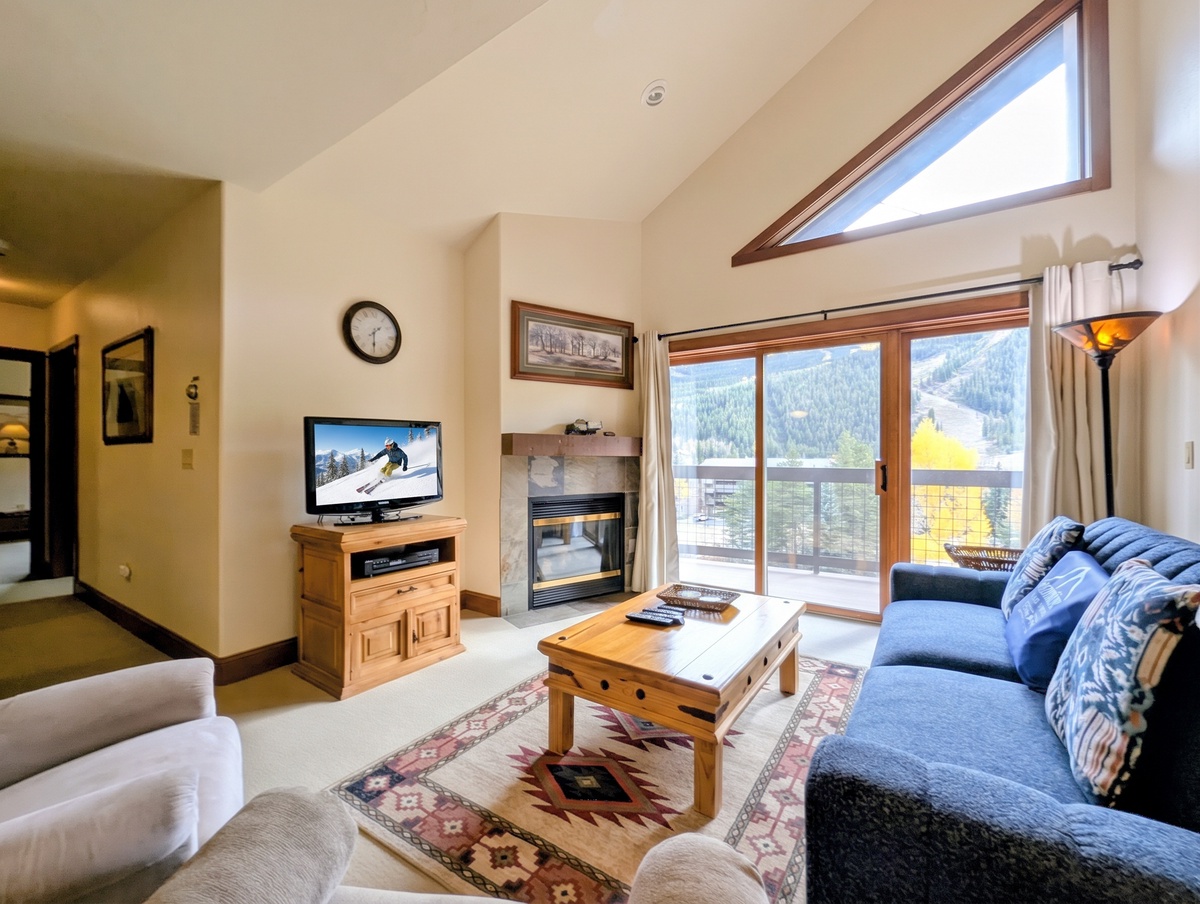 Unwind in your bright, airy living room with soaring ceilings and a cozy fireplace, where stunning mountain views stretch across the horizon beyond your private balcony.