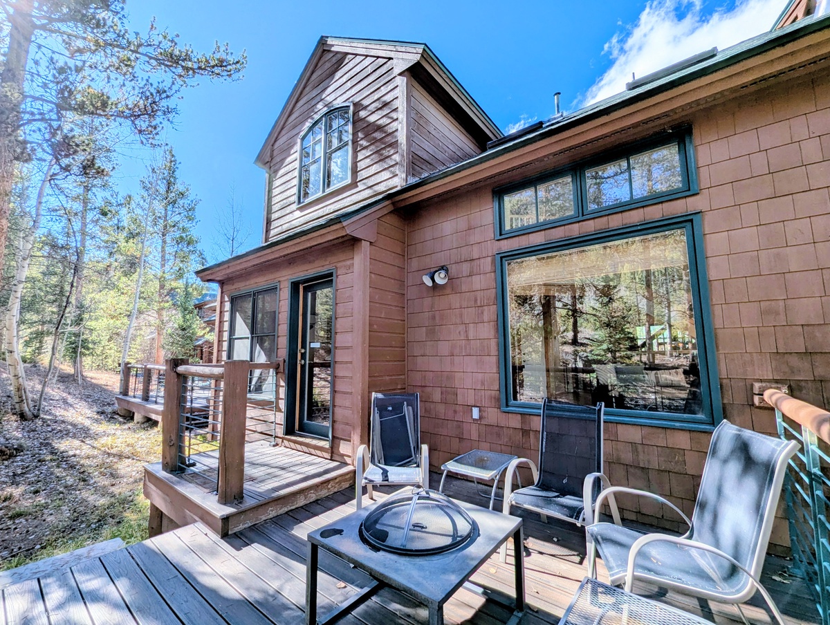 Private deck with fire pit and seating, nestled among towering pines under a bright blue sky—a perfect spot to unwind after exploring the surrounding area.