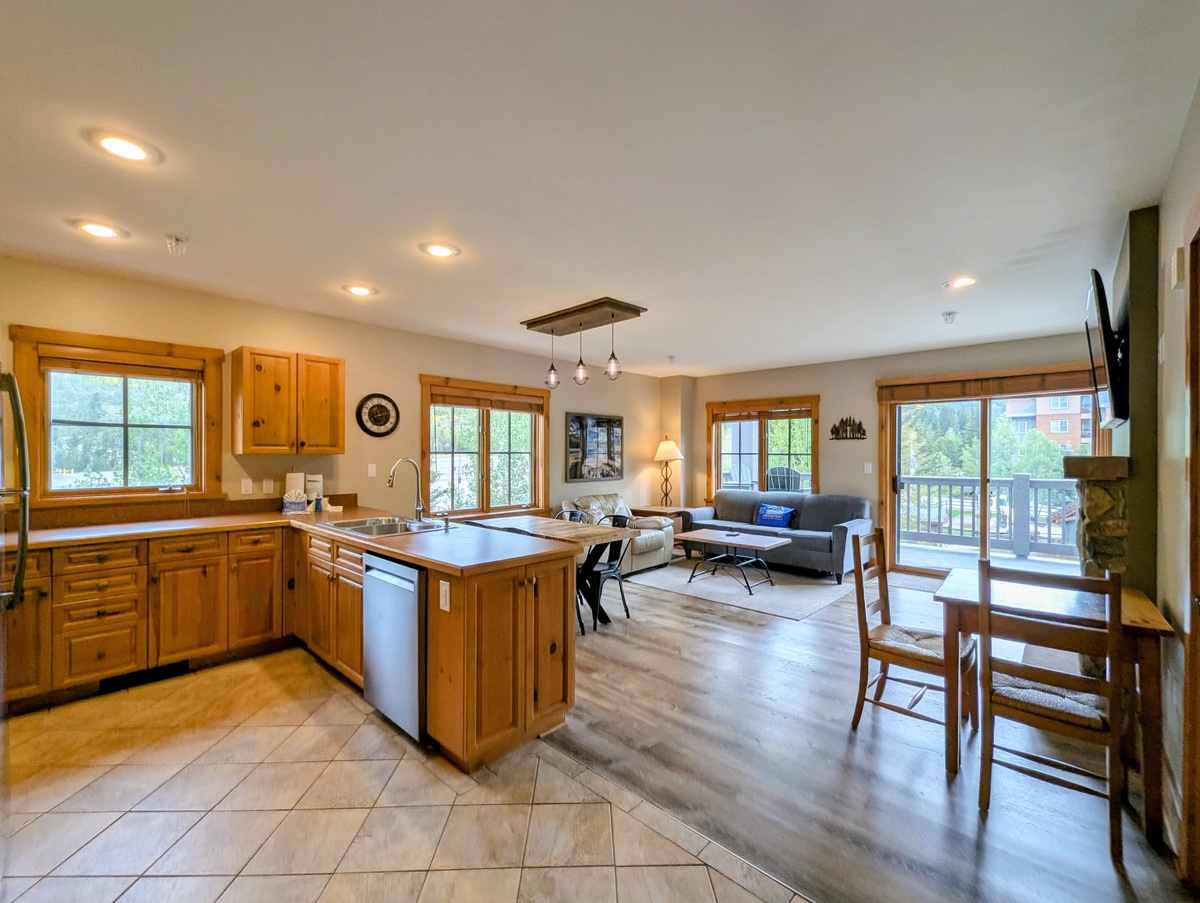 Bright, open-concept space with warm wood tones and modern comforts. Sunlight streams through multiple windows, illuminating the fully-equipped kitchen and inviting living area perfect for cooking and relaxing.