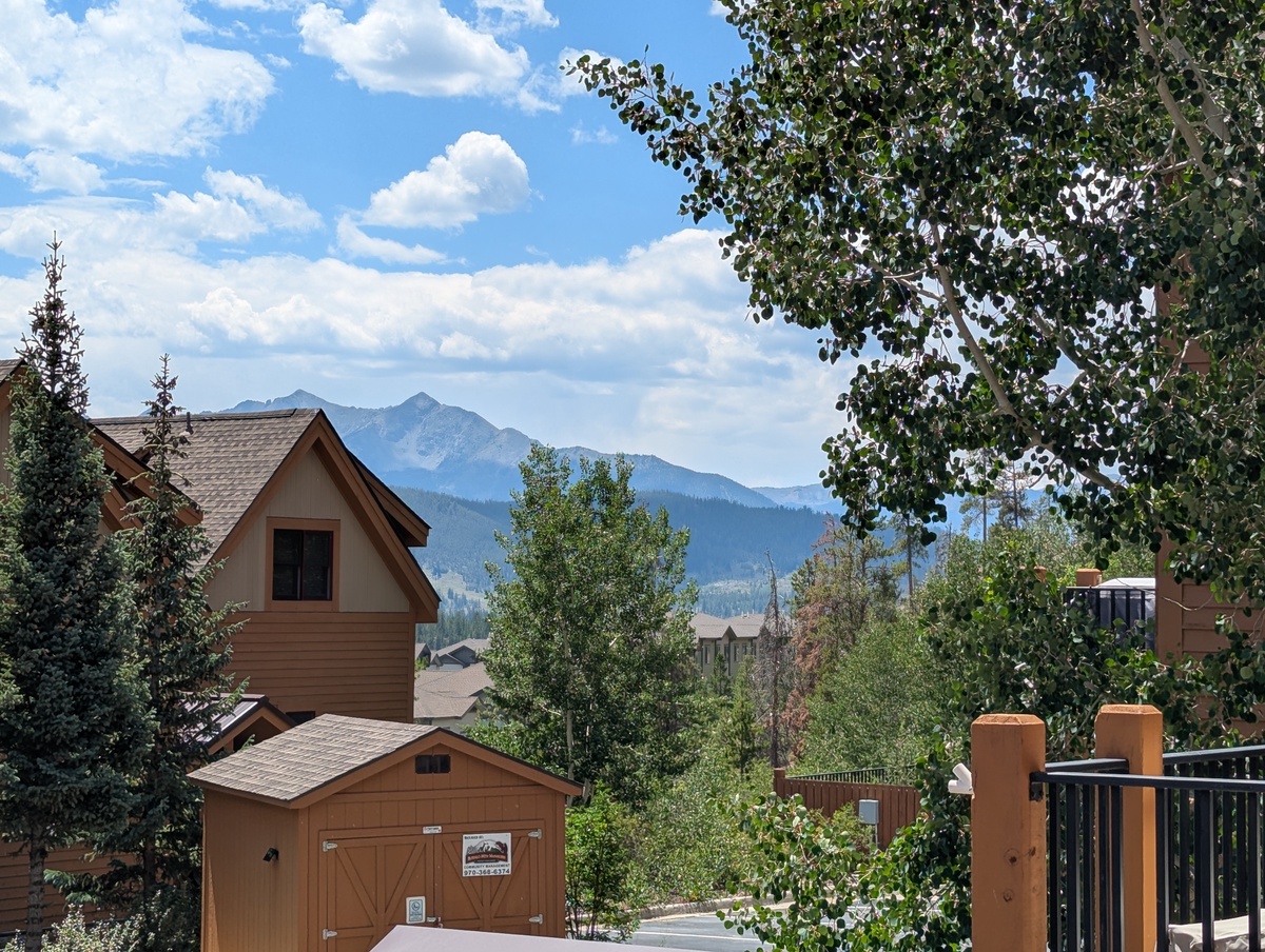 A mountain retreat nestled in nature, with towering peaks framing the property and leafy trees lending shade and serenity to the surrounding neighborhood.