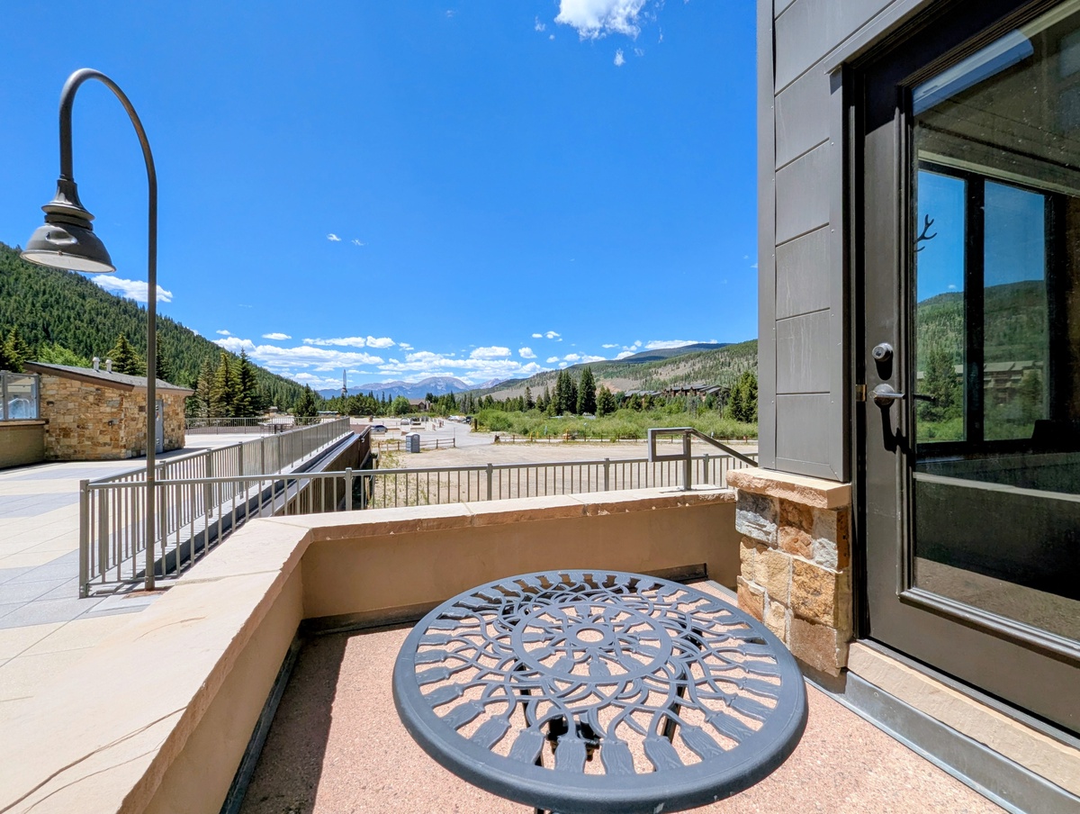 The property features a private balcony with mountain scenery and outdoor seating, located in a pedestrian-friendly neighborhood with forested hillsides, convenient walkways, and nearby local amenities.